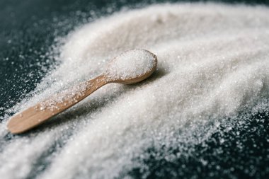 Siyah arka planda tahta kaşık dolusu şeker, sıçrama.