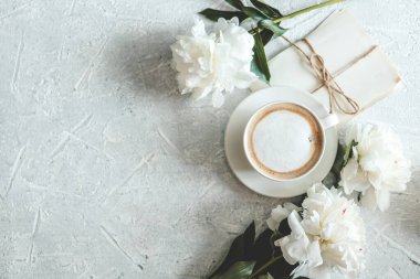 Yaz kompozisyonu üst görünümü. Bir fincan kahve, şakayık ve gri arka planda klasik mektuplar..