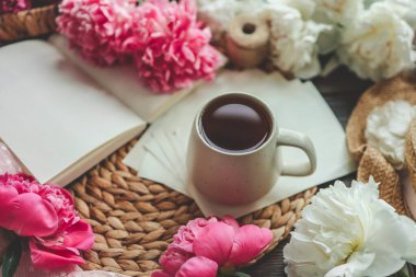 Güzel bahar kompozisyonu, günaydın konsepti. Bir fincan çay, şakayık ve açık bir kitap..