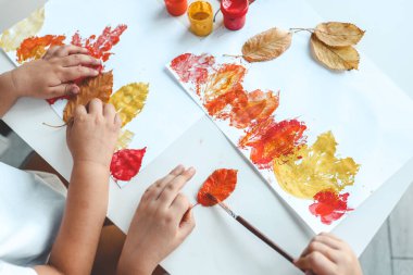 Çocuklar yaprakları boyar ve bir baskı yapar, sonbahar yaratıcılığı..