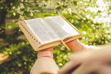 Girl with the Bible in her hands in the spring garden. clipart