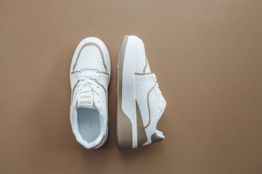 Bej arka planda şık beyaz spor ayakkabılar, üst görünüm.