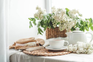 Pencere kenarında çay ve çaydanlık ve beyaz leylaklı sepet, günaydın konsepti..