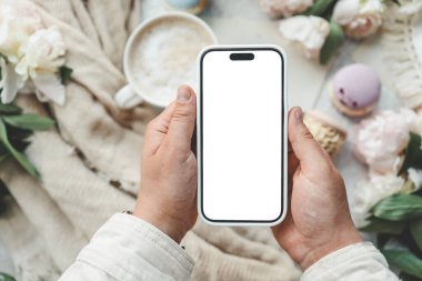 Bir fincan kahvenin arka planında izole bir ekran olan telefon elinde..