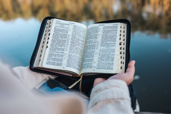 Girl reading the Bible on the river bank.