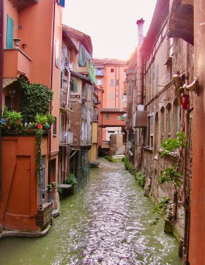 Blue-green water in stone lined canal in Italy with small boats moored along the shore                          