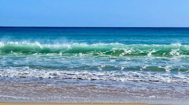 Sahilde dalgalar ve ufukta açık gökyüzü olan güzel bir deniz manzarası.