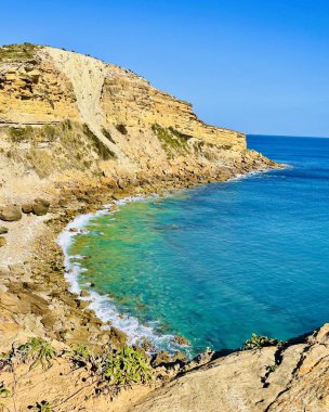 Sakin mavi ve turkuaz okyanus suyu, Burgau Portekiz yakınlarındaki yüksek bir uçurumun altında yavaşça süzülür..
