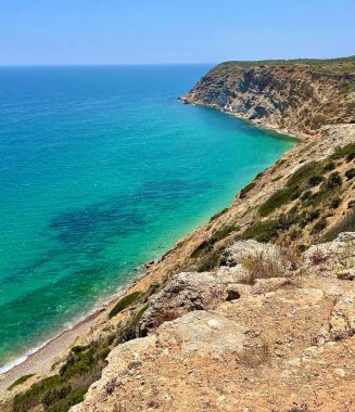 Berrak mavi suları olan kayalık bir sahil manzarası