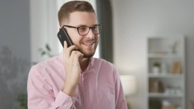 Gözlüklü gülümseyen yakışıklı iş adamı akıllı telefon tutuyor ve konuşuyor, sorunları uzaktan çözüyor. İş görüşmesi konsepti, başarı.