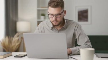 Laptop kullanan konsantre genç adam, uzaktan ders sırasında notlar alıyor. Öğrenci evde internetten bilgisayar ekranına bakıyor.