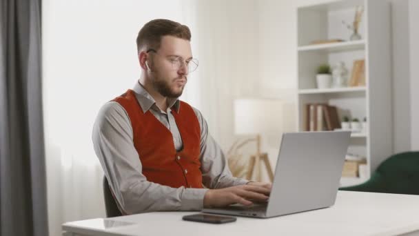 年轻英俊的男人戴着眼镜 用笔记本电脑 键盘打字 和同事聊天 听音乐 成功的自由职业者在网上电脑上工作 — 图库视频影像
