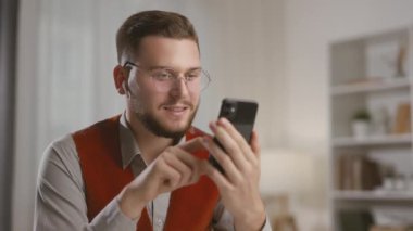 Akıllı telefon tutan ve sosyal medyayı kontrol eden, internetten sipariş veren veya evde otururken gülümseyen genç adam