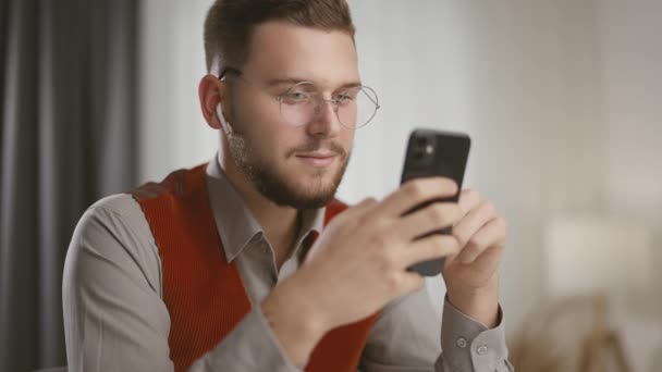 Счастливый Улыбчивый Мужчина Очках Смотрит Экран Смартфона Пользуется Мобильными Приложениями — стоковое видео