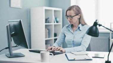 Ofis çalışanı bilgisayar kullanarak ofiste çalışan neşeli, güler yüzlü bir kadın.