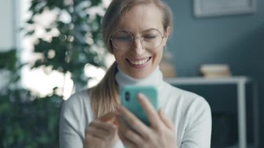 Evde akıllı telefon kullanan olgun bir kadın, gülümseyen sarışın kadın online alışveriş uygulaması kullanıyor.