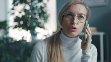 Neşeli olgun bir kadın akıllı telefonuyla konuşuyor, sarışın bir kadın cep telefonuyla evden konuşuyor, manzarayı kapatıyor.