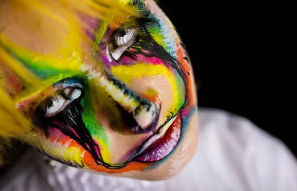 Close up view of woman with yellow hair and evil clown face art on black background