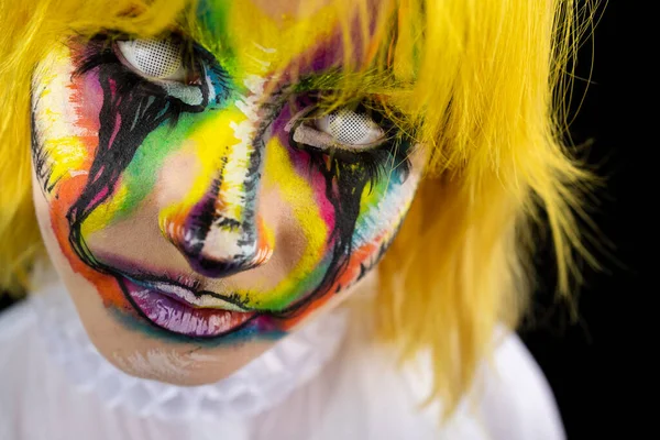 Close up view of woman with yellow hair and evil clown face art on black background