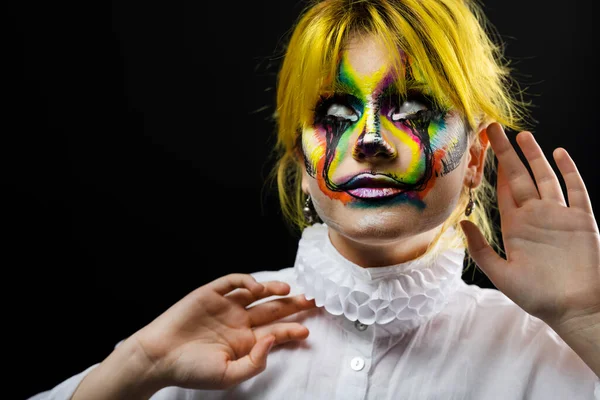 Portrait of woman with yellow hair and evil clown face art posing on black background