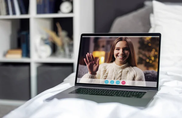 白いリネンの快適なベッドの上に立つ若い女性とノートパソコン 陽気な女性は ビデオ通話中に手を振って 自宅で現代的なガジェットを使用しています 技術接続の概念 — ストック写真