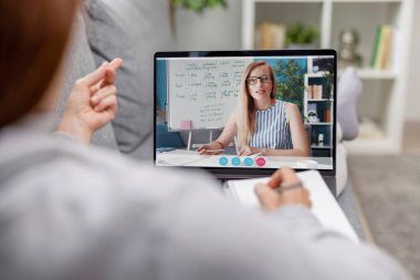 Olgun bir kadının rahat kanepesinde kablosuz bilgisayardan ders dinlemesi. Bayan oturma odasının içinde İngilizce öğreniyor.