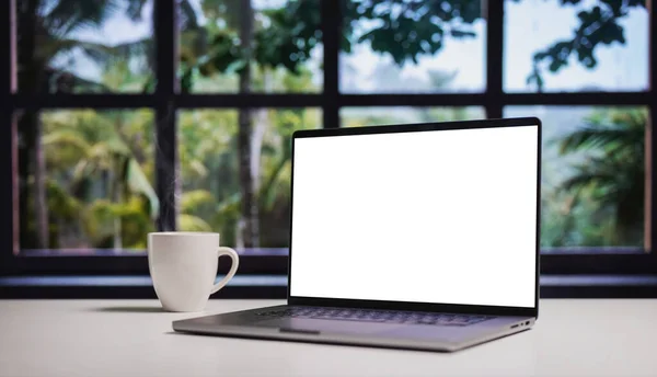 Modern laptop with blank white screen for copy replacement, cozy home interior with wide forest window view