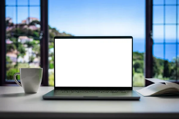 具有空白白色屏幕的现代笔记本电脑 可更换副本 舒适舒适的家庭内部 有宽阔的海滨窗口视野 免版税图库照片