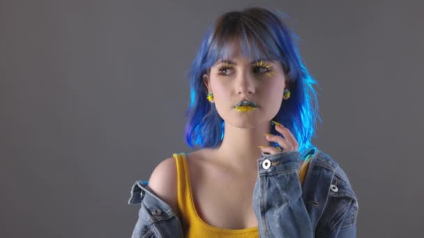 Молодая Стильная Женщина Синих Желтых Тонах Одежды Позирует Сером Фоне — стоковое видео