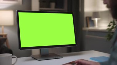 Mature bearded man working on personal computer at home, cozy evening typing on keyboard, close up of green chromakey monitor