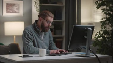 Evde bilgisayar başında çalışan olgun yakışıklı bir adam, rahat bir akşam odasında kod yazan sakallı bir programcı.