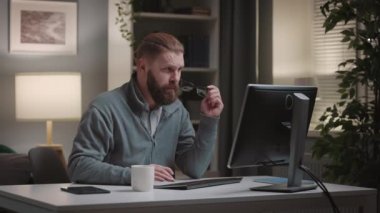 Mature handsome man working on pc at home, bearded thoughtful programmer writing code in cozy evening room