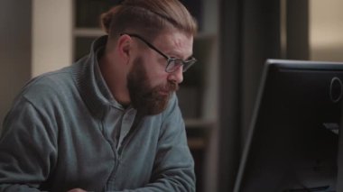 Focused bearded man working on computer at home, mature businessman has thoughts before monitor