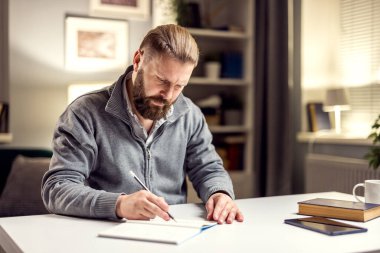 Kendine güvenen olgun bir adam not defterine notlar alır, akşam vakti oturma odasında oturur.