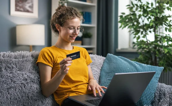 快乐的卷曲女人穿着黄色的衬衫 用笔记本电脑在网上购物 从家里购物 免版税图库照片