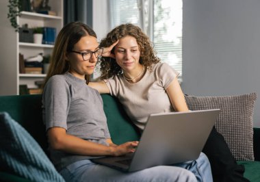 İki genç kadın dizüstü bilgisayar kullanıyor, evde boş zaman geçiriyor, eğlenceli bir konsept.