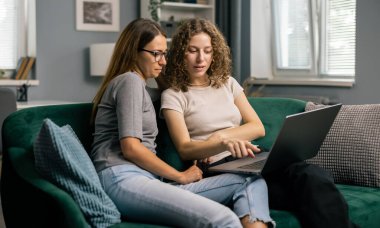 İki genç kadın dizüstü bilgisayar kullanıyor, evde boş zaman geçiriyor, eğlenceli bir konsept.