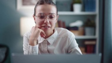 Gözlüklü ve beyaz gömlekli gülümseyen kadın laptopta neşeli bir görüntülü sohbet yapıyor.