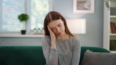 Genç, yorgun bir kadın kanepede baş ağrısı ve stres hisseder. Güzel bir odada yastıklar, yakın çekim.