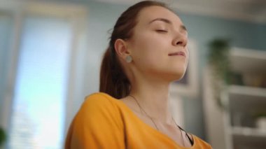 Yoga yapan genç bir kadının yakın plan yüzü rahat bir odada gözleri kapalı nefes alma egzersizleri yapıyor, göz kapaklarını açarak alıştırmayı bitiriyor.