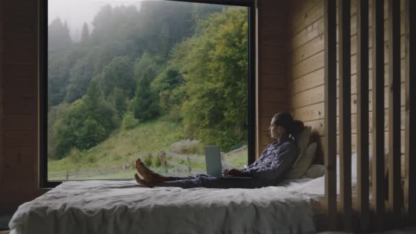 快乐的女人在有宽阔窗户的卧室里工作 身后森林里的雾蒙蒙的早晨 平静的闲暇时间概念 — 图库视频影像