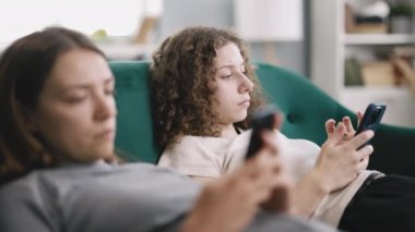 İki sıkılmış kadın kanepede, akıllı telefonlara bakıyor ve birbirlerini görmezden geliyorlar, gün boyunca evde yalnız hissediyorlar.