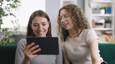 Gözlüklü gülümseyen kadın ve gri tişörtlü bayan arkadaş tablette görüntülü sohbet edin ve günün nasıl geçtiğini anlatın.
