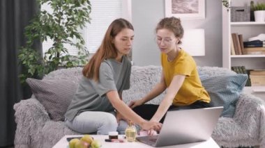 İki güzel bayan arkadaş kozmetik hakkında konuşuyor, masadaki rahat koltukta dizüstü bilgisayarla oturuyor ve internette makyaj alışverişi yapıyorlar.