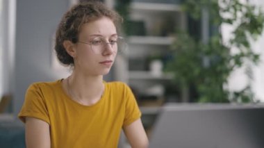 Gülümseyen genç bir kadın işçi, evden online bir iş, dizüstü bilgisayarda bilgi arıyor ve düşünceli bir şekilde her şeyi okuyor.
