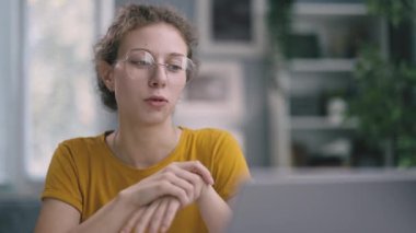 Gözlüklü ve sarı tişörtlü gülümseyen kadın laptopta görüntülü sohbet eder, iş planlarını iş arkadaşlarıyla tartışır, arkadaşlarıyla haber yapar.
