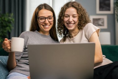 İki kadın arkadaş görüntülü sohbet ediyor, günü tartışıyor ve rahat bir dairede dizüstü bilgisayarda iyi vakit geçiriyor, kahve içiyor ya da lezzetli bir çay içiyor.