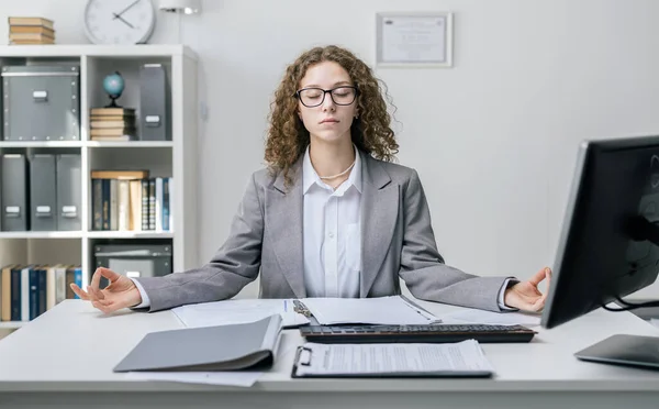 Young businesswoman practice yoga at computer desk, tired worker in white shirt and grey jacket engages in breathing exercises in office