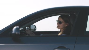 Göz kamaştırıcı gözlüklü genç bir kadının portresi arabayı hareketli ve güneşli şehirde gezdirirken aynaya bakarak, görüntüden yansıtılır.