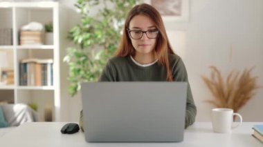 Genç ve neşeli bir iş kadını, bilgisayarını kullanarak, rahat ve rahat bir daireden uzak bir işte çalışırken portrede yakalandı.